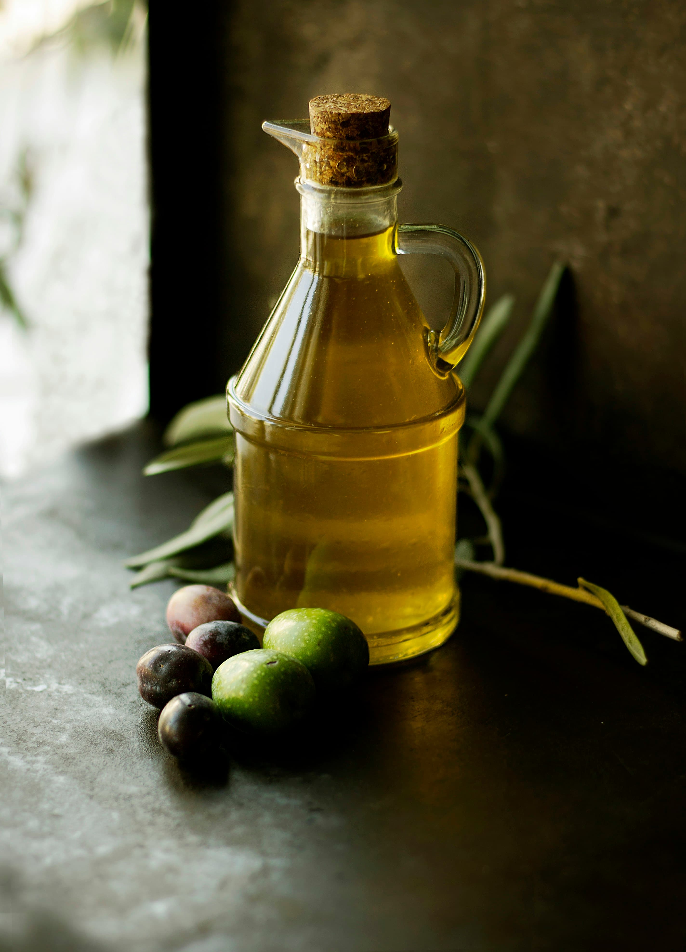 Olive oil in a glass bottle beside fresh olives